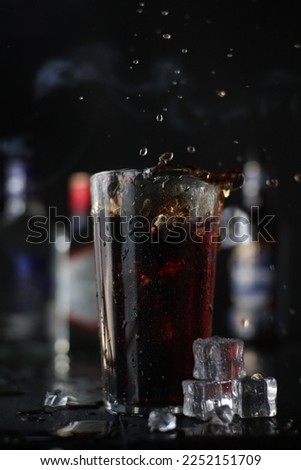 Pouring beer in the glass. Beer with dark background. Ice cubes around the glass