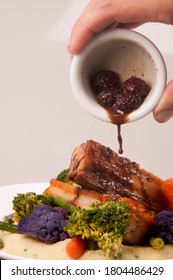 Pouring Berry Sauce Over A Pork Meat In A Dish In Gray Background - Isolated Front View