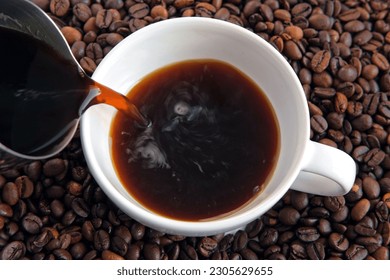 Pouring black coffee into white ceramic cup. Top view. Close up. Hot coffee drink pour into cup from shiny moka pot coffee maker. Roasted coffee beans background. Freshly brewed Espresso, americano. - Powered by Shutterstock