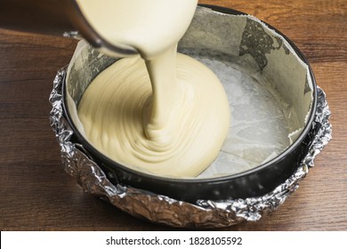Pouring cake mixture into a cake tin line with paper and wrap with aluminum foil for baking cheesecake.