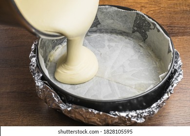 Pouring cake mixture into a cake tin line with paper and wrap with aluminum foil for baking cheesecake.