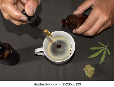 Pouring CBD tincture in a coffee cup, natural remedy of marihuana. Person using cannabis oil with a dropper in a table with marihuana leaf.