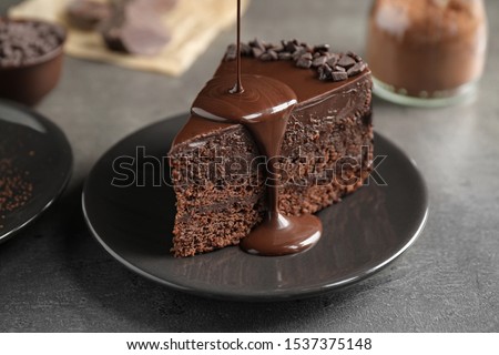 Pouring chocolate sauce onto delicious fresh cake on grey table, closeup