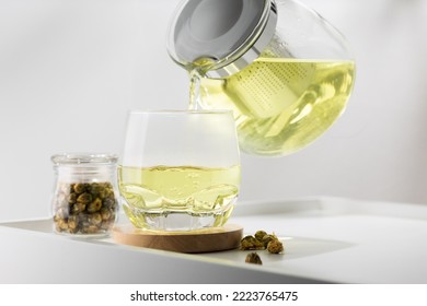 Pouring chrysanthemum hot tea into glass on the white table