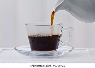 Pouring Coffee Into A Half Full Clear Cup With A Saucer.