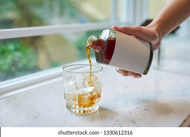 Pouring Cold Brew Coffee From A White Label Bottle, Into A Half Filled, Icy Glass.