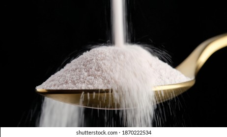 pouring collagen powder in golden spoon on black background closeup. Natural beauty and health supplement