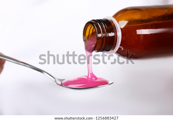 Pouring cough syrup into spoon on white\
background, closeup
