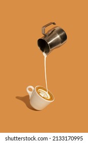 Pouring creamy milk from a stainless steel milk jug, and making late art espresso in a coffee cup on brown background. - Shutterstock ID 2133170995