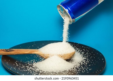 Pouring Crystal Sugar From A Blue Aluminum Can To A Wooden Spoon On A Black Plate And Light Blue  Background.  Motion Blur On Sugar Texture. Sugar Danger Concept