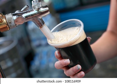 Pouring dark beer to plastic glass from beer tap - Powered by Shutterstock