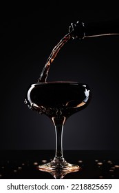 Pouring Dark Soda Into Champagne Glass On Black