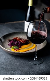 Pouring deep red wine in a wine glass on fire ground, beautiful macro flow from bottle, dark grey elegant photo with bright accents