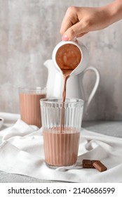 Pouring Of Delicious Chocolate Milk From Jug Into Glass On Grunge Background