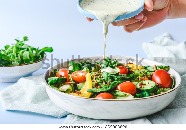 Pouring Dressing on Garden Salad on a light\
green cloth and light blur\
background