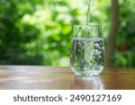 pouring drinking water in to clear glass on wooden table in garden background. 