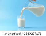 Pouring fresh milk into the glass on light blue background.