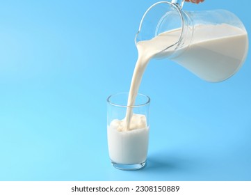 Pouring fresh milk into the glass on light blue background. - Shutterstock ID 2308150889