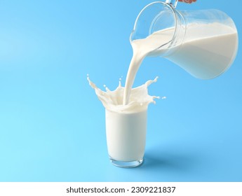 Pouring fresh milk into the glass with splashing on light blue background.