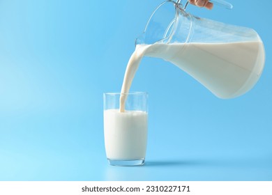 Pouring fresh milk into the glass on light blue background. - Shutterstock ID 2310227171