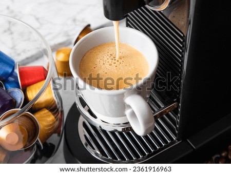 Pouring fresh morning coffee with espresso machine and capsules pods on white marble.