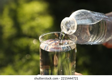 Pouring Fresh Water From Bottle Into Glass Outdoors, Closeup