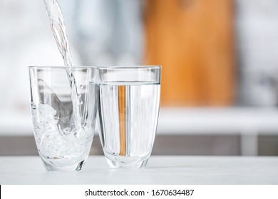 Pouring Of Fresh Water Into Glass On Table In Kitchen