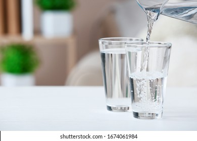 Pouring Of Fresh Water Into Glass On Table In Room