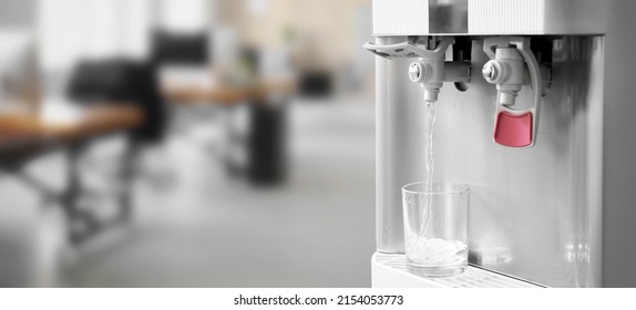 Pouring of fresh water from modern cooler into glass in office, closeup - Shutterstock ID 2154053773