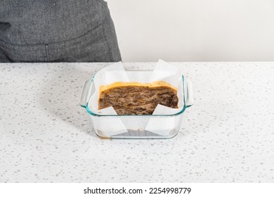 Pouring fudge mixture into the baking pan lined with parchment paper to prepare chocolate peanut butter fudge. - Shutterstock ID 2254998779