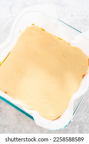Pouring fudge mixture into the square glass baking pan lined with parchment paper to prepare candy corn fudge. - Shutterstock ID 2258588589