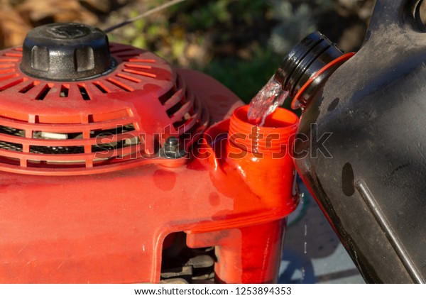 Pouring gasoline\
into the tank of  lawn\
mower.