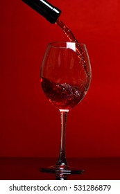 pouring glass with beautiful stream of red wine on red background, side view