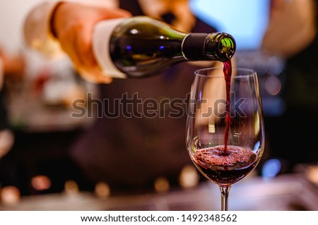 Pouring glass of red wine from a bottle.