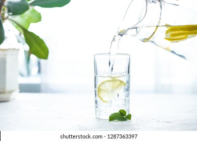 Pouring a glass of water with lemon, ice and mint on a white table - Powered by Shutterstock