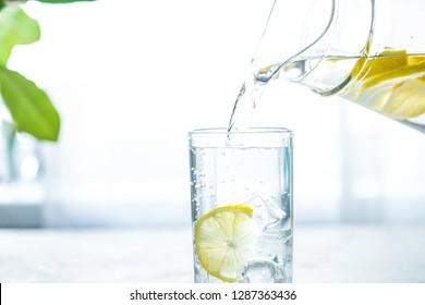 Pouring a glass of water with lemon, ice and mint on a white table - Powered by Shutterstock
