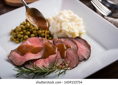 Pouring Gravy Sauce On Sliced Roasted Beef With Mushed Potato And Sweet Peas