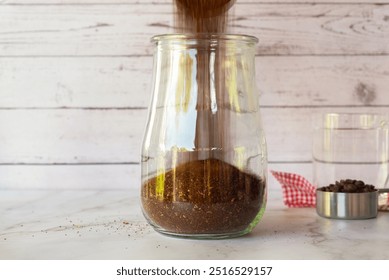 Pouring ground coffee into a glass jar, how to make cold brew coffee at home step by step. - Powered by Shutterstock