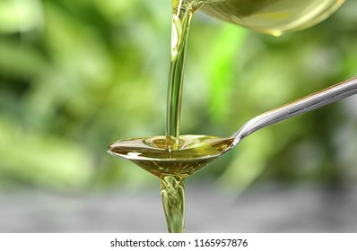Pouring hemp oil into spoon on blurred background, closeup