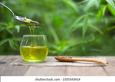 Pouring hemp oil into spoon and hemp seeds in a wooden spoon on a green hemp leaf background, CBD Hemp oil.