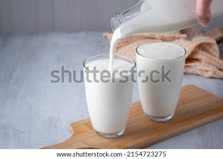 Pouring homemade kefir, buttermilk or yogurt with probiotics. Yogurt flowing from glass bottle on light background. Probiotic cold fermented dairy drink. Trendy food and drink. Copy space.