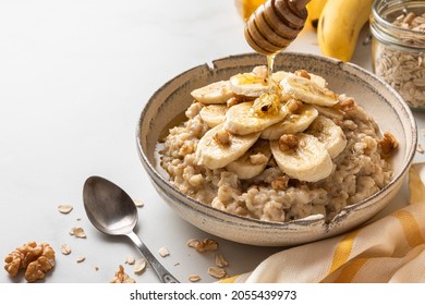 Pouring honey in a bowl of oatmeal porridge with banana and walnuts. Healthy diet breakfast. Close up - Powered by Shutterstock