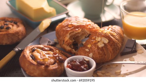 Pouring Honey Over A French Breakfast With Pastries, Orange Juice And Chocolat