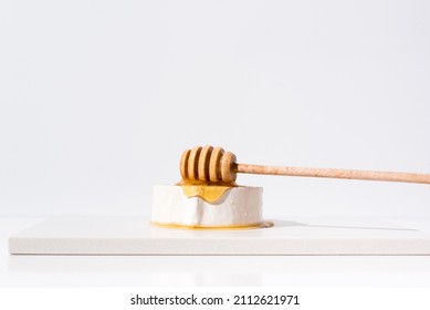 Pouring Honey Over A Piece Of Creamy Goat Cheese On A White Table