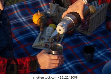 Pouring hot beverage from a thermos into a cup during an outdoor picnic, with copy space. - Powered by Shutterstock