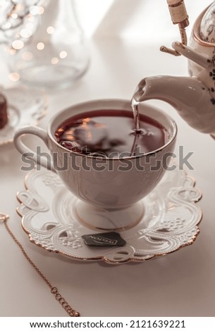 Pouring hot cherry tea from teapot into porcelain cup
