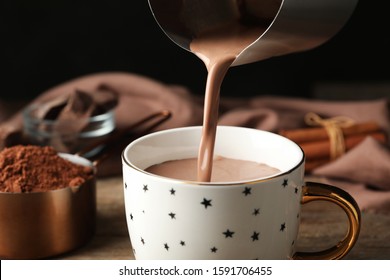 Pouring hot cocoa drink into cup on wooden table