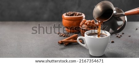 Pouring of hot coffee from cezve into cup on table