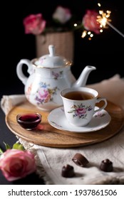 pouring hot steaming tea from a vintage teapot into glass cups on a black background with chocolate candies, roses and sparkling lights