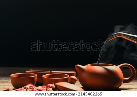 Pouring hot water into a clay tea jug for fragrant red rose tea. Placed on old wood with black background